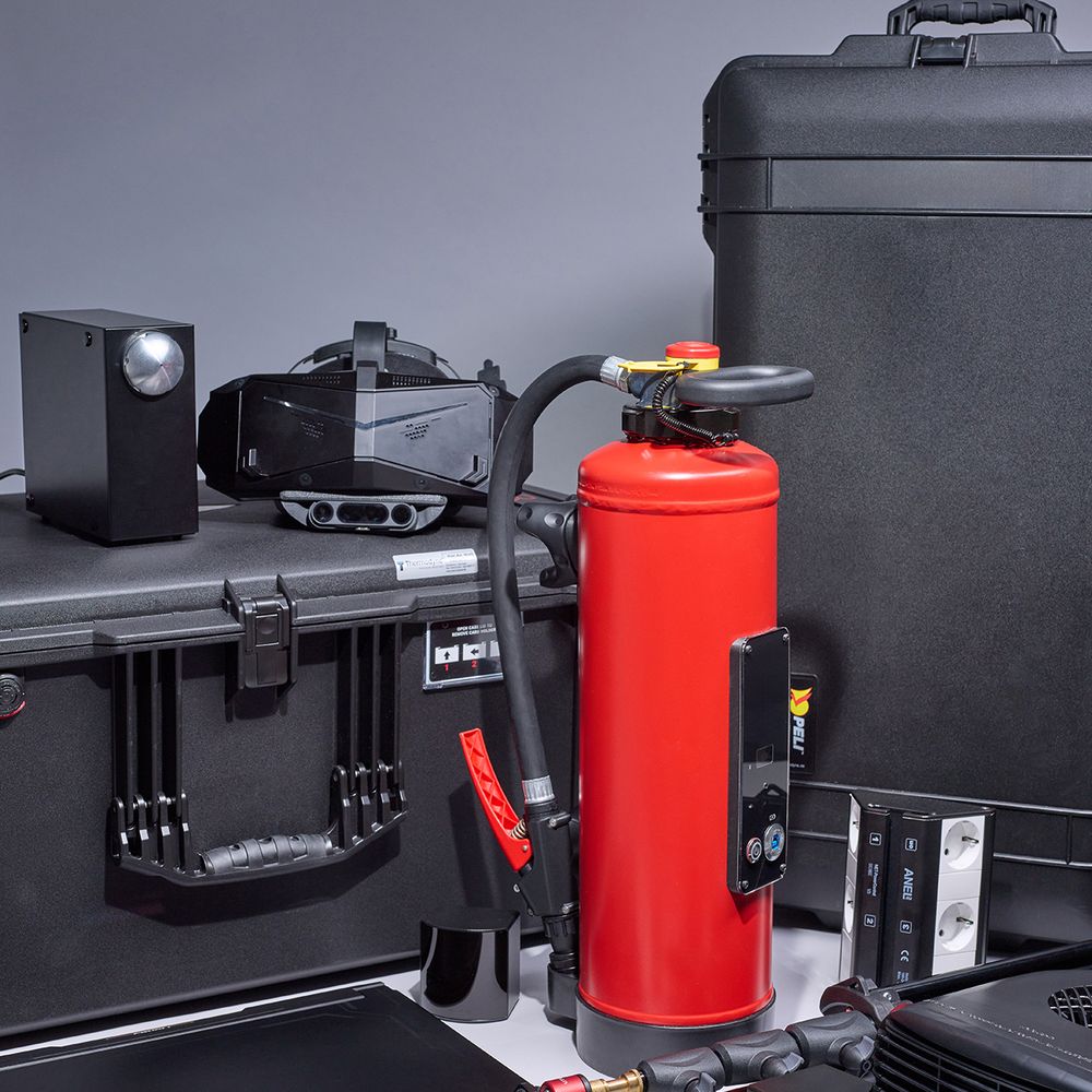 A collection of black equipment cases, a red fire extinguisher, and various electronic devices arranged against a gray background.