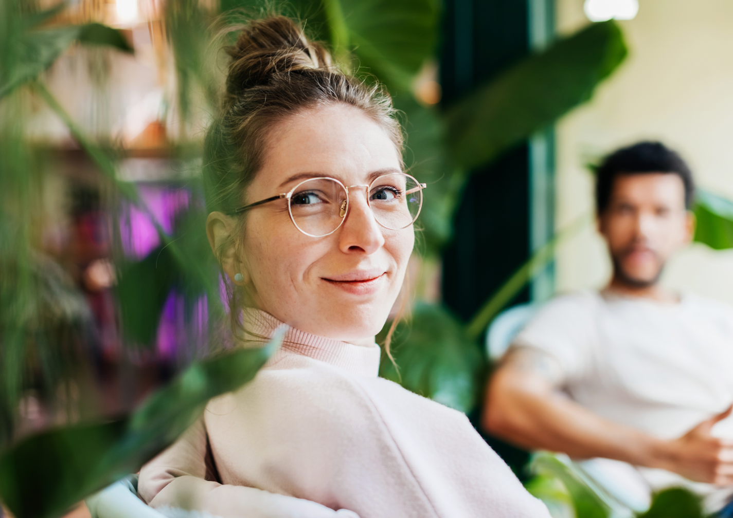 Frau sitzt vor Pflanzen und schaut in die Kamera