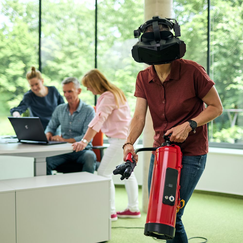 Frau bei virtuellem Löschvorgang mit einer VR Brille und einem Feuerlöscher in der Hand.