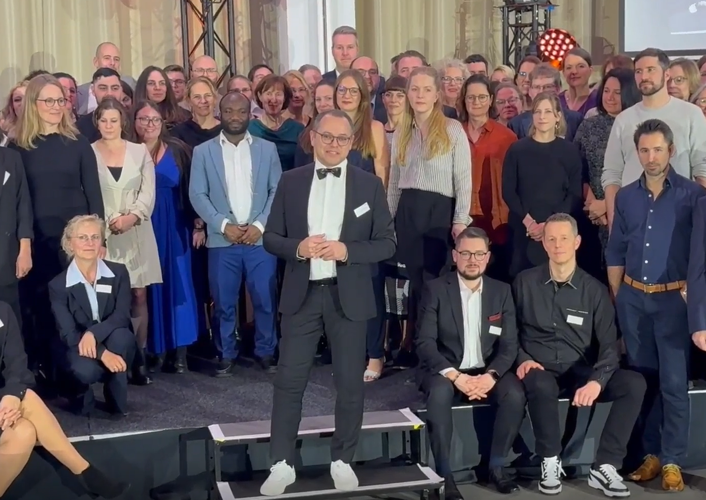 Prof. Dr. Thomas Auhuber steht vor einer großen Gruppe Absolventen