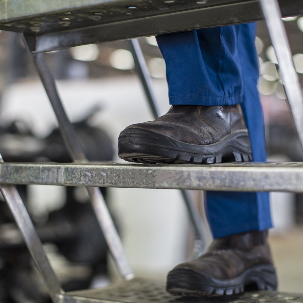 Person mit Sicherheitsschuhen steigt eine industrielle Metalltreppe hinauf.