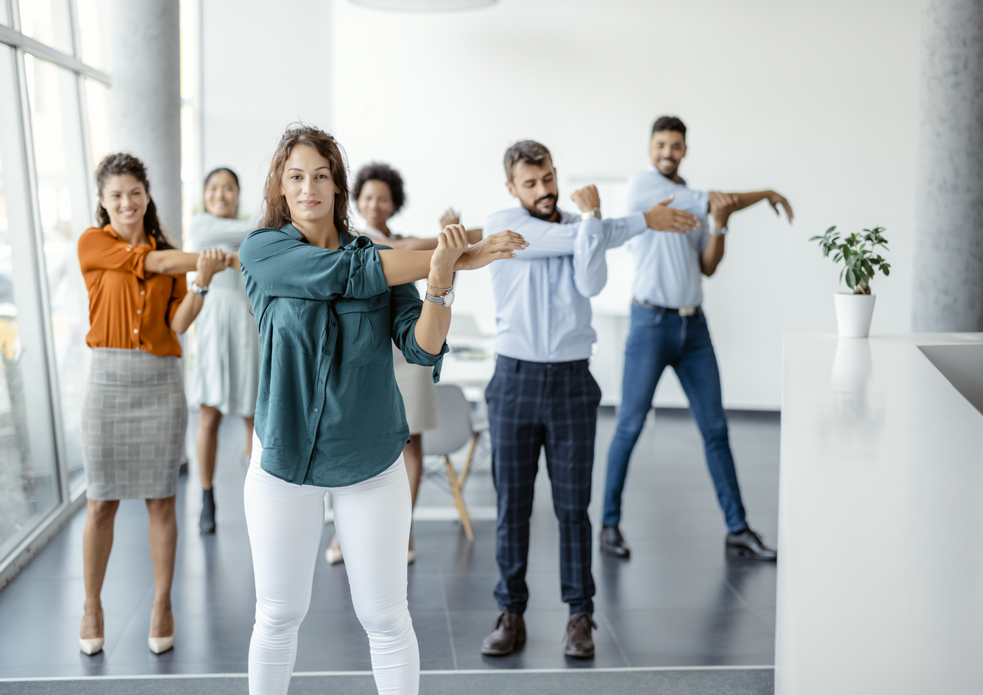Gruppe von Büroangestellten führt gemeinsame Dehnübungen für die Arme durch.