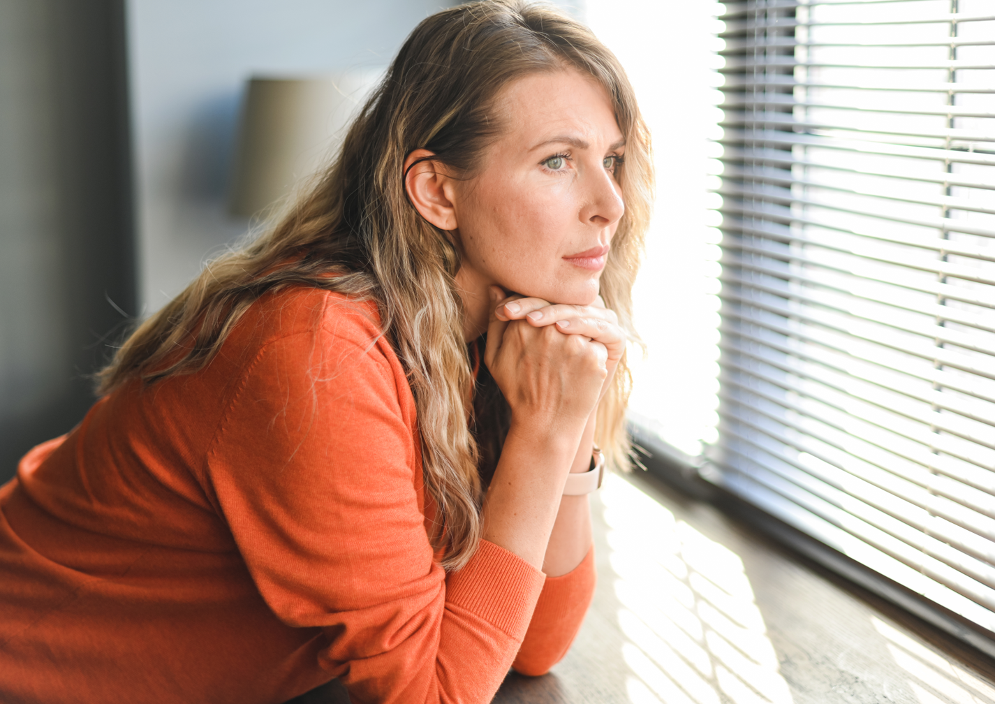 Frau steht am Fenster und guckt nachdenklich raus