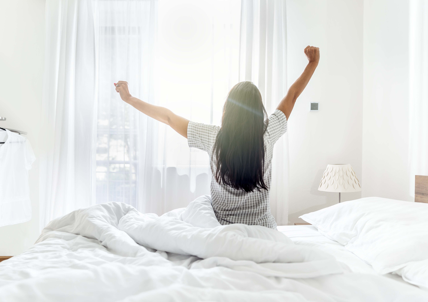 EIne Frau streckt sich, sitzend im Bett mit den Rücken zugewandt und wacht vermutlich gerade auf