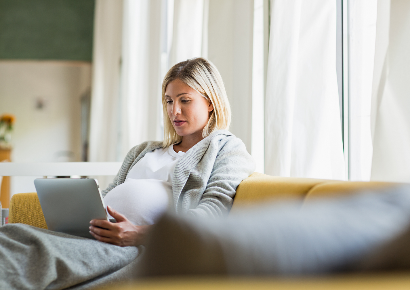 Schwangere Frau sitzt auf einem Sofa und benutzt ein Tablet.