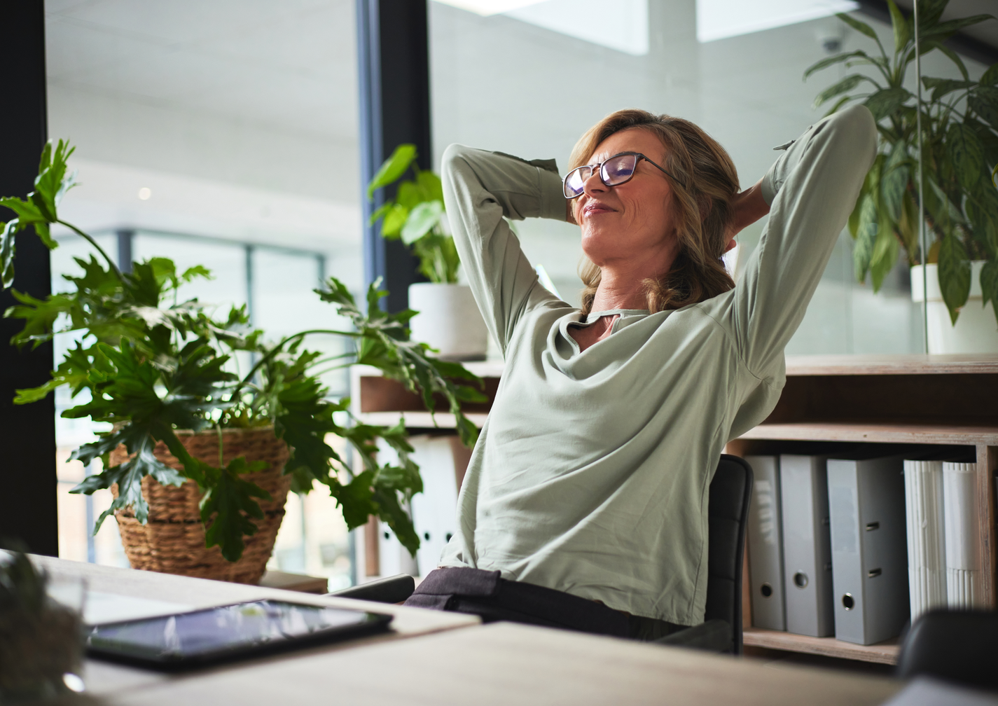 Frau in einem modernen Büro lehnt entspannt im Stuhl zurück, umgeben von Pflanzen.