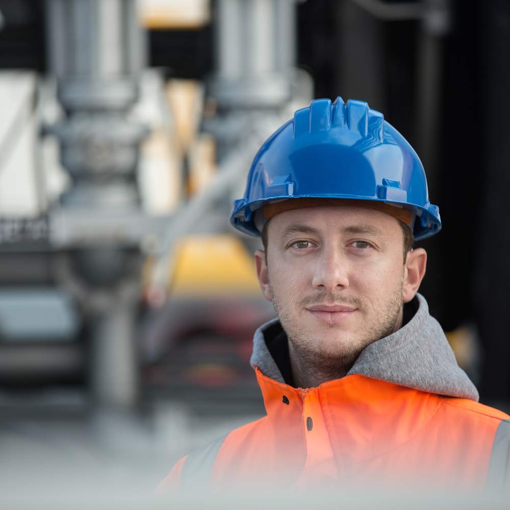 Bauarbeiter in orangener Jacke und blauem Helm auf einer Baustelle.