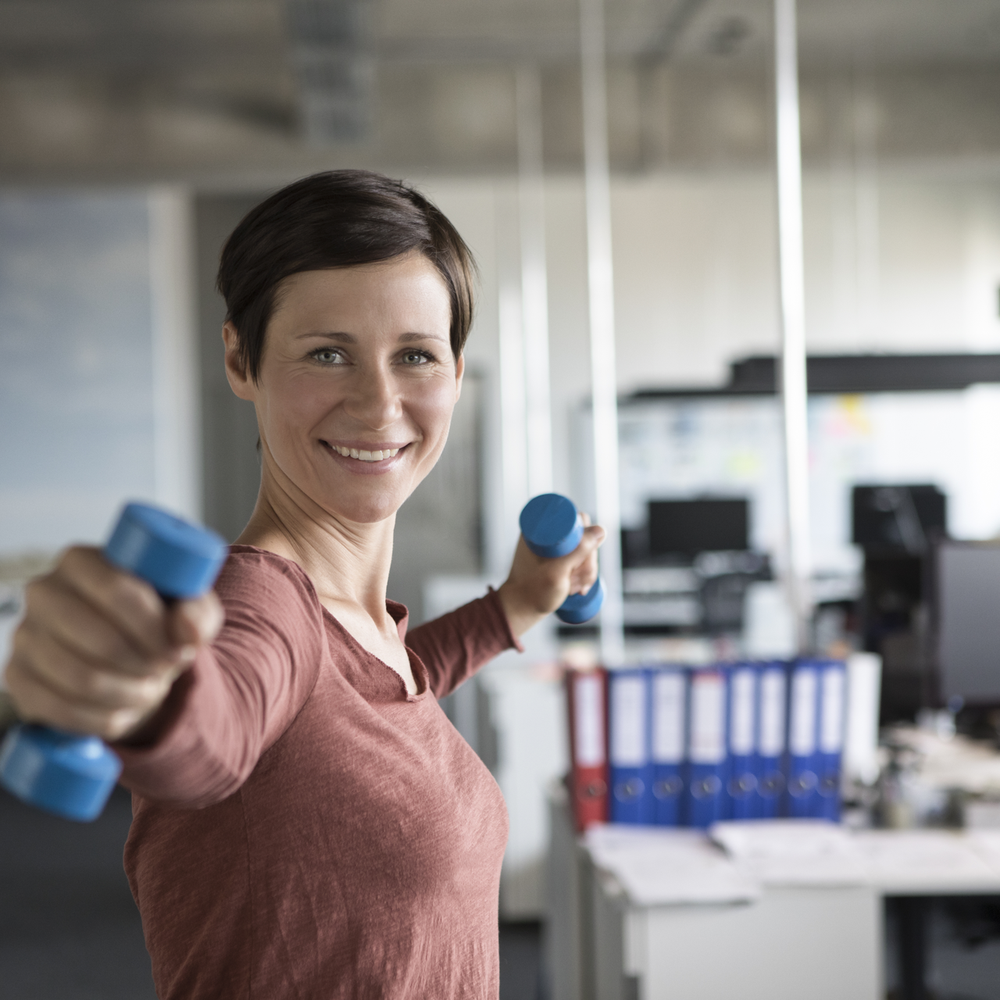 Eine Frau trainiert mit kleinen Hanteln in einem modernen Büro.