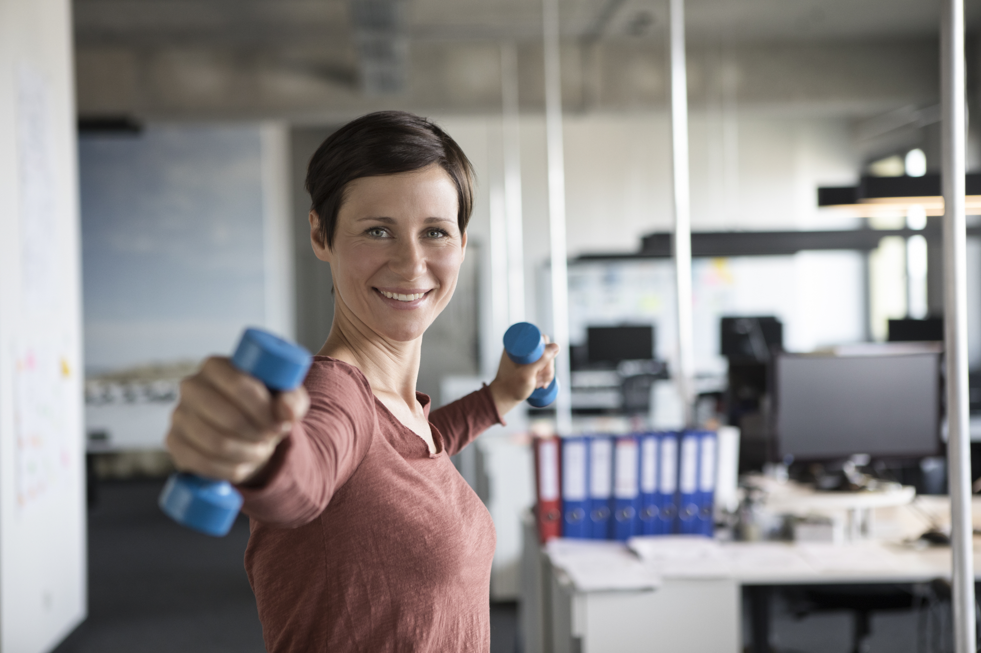 Eine Frau trainiert mit kleinen Hanteln in einem modernen Büro.