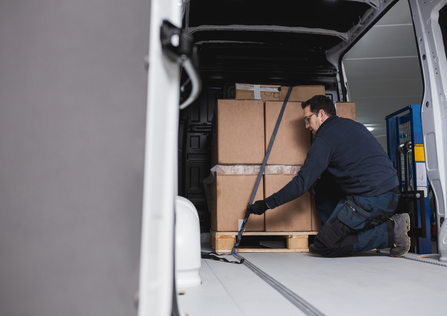 Mann sichert Kartons im Transporter mit einem Spanngurt.