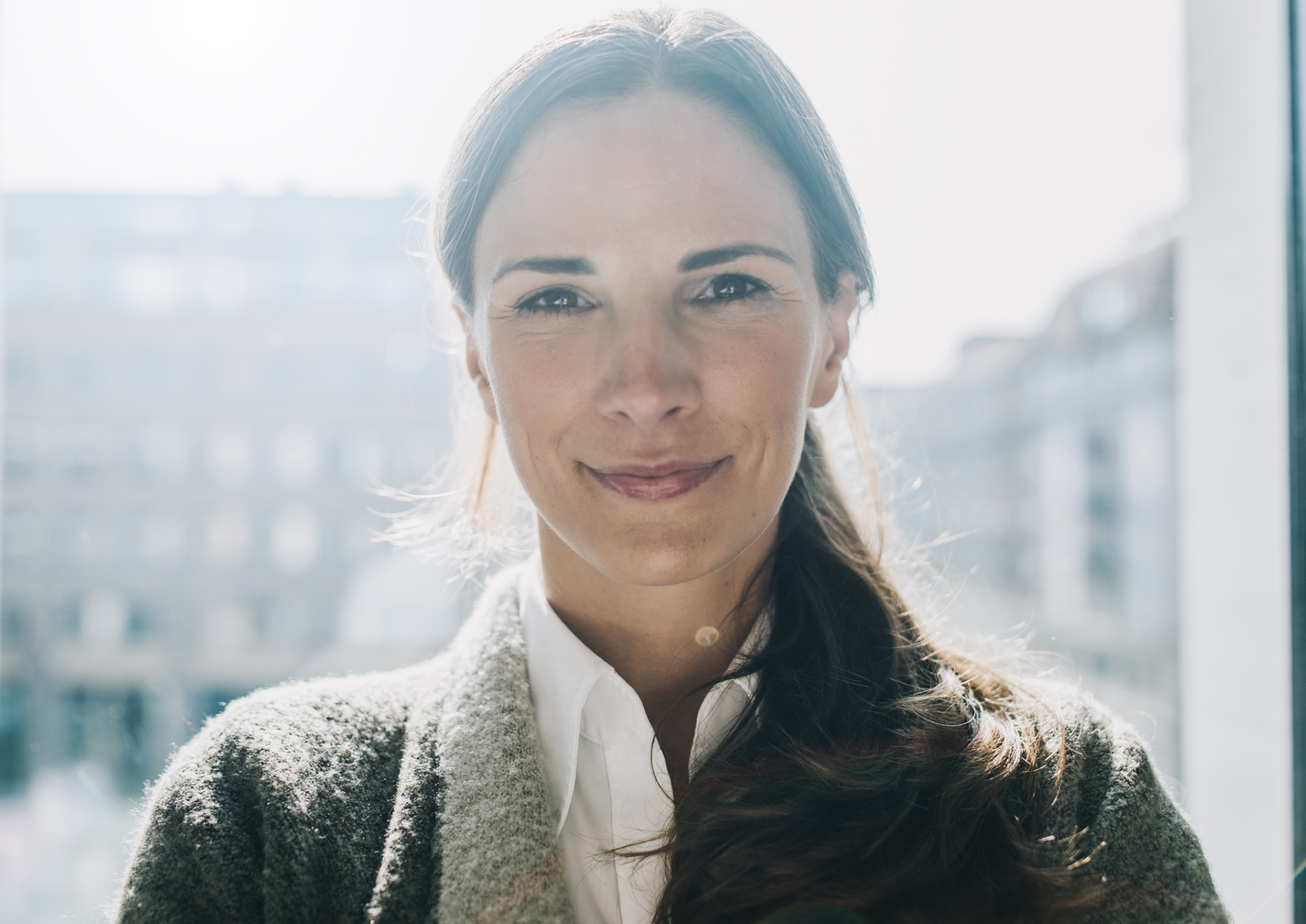 Porträt einer Frau mit freundlichem Ausdruck vor einem Fenster.