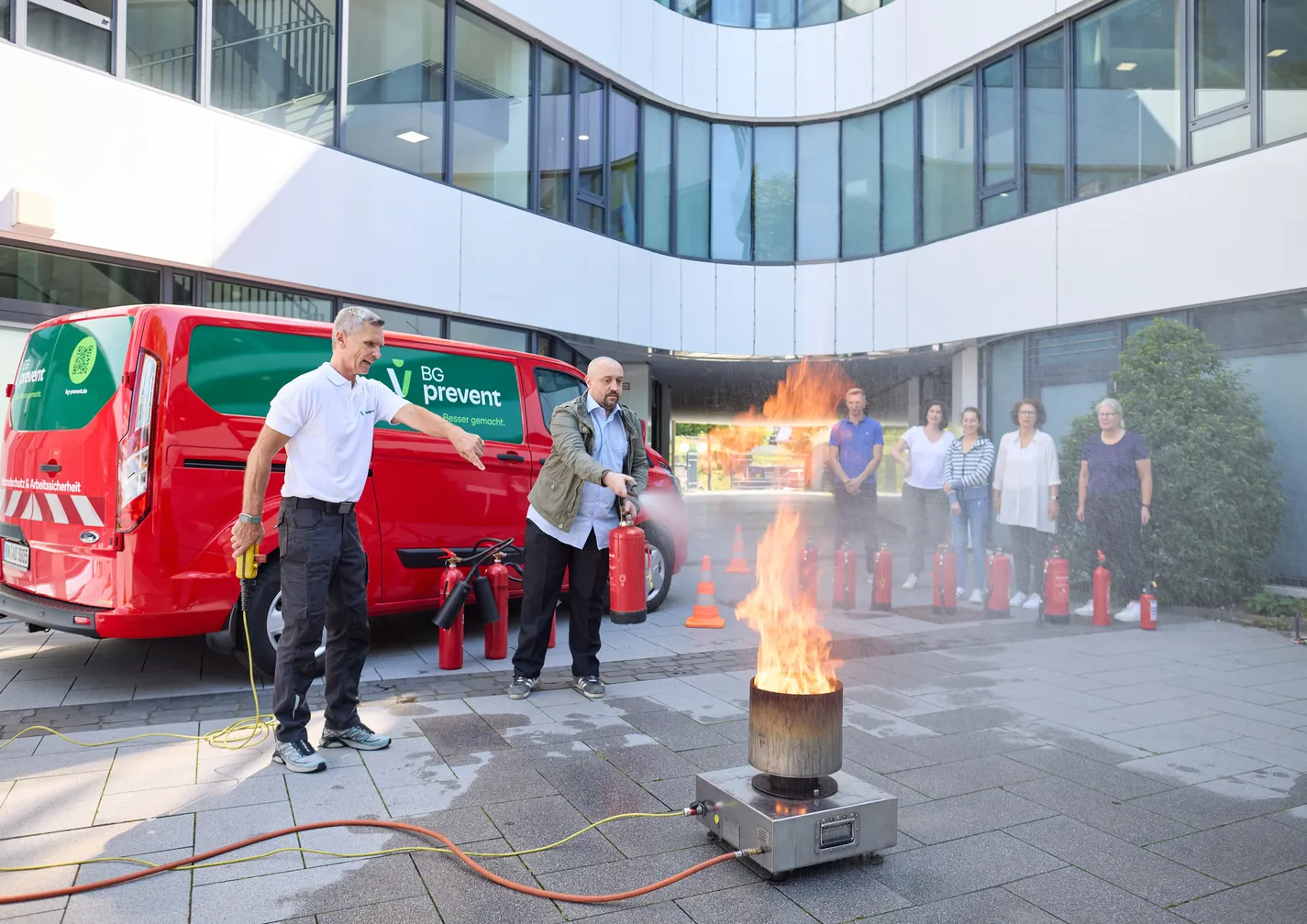 Brandschutzübung vor Bürogebäude: Teilnehmer lernen unter Anleitung den sicheren Umgang mit Feuerlöschern im Ernstfall.