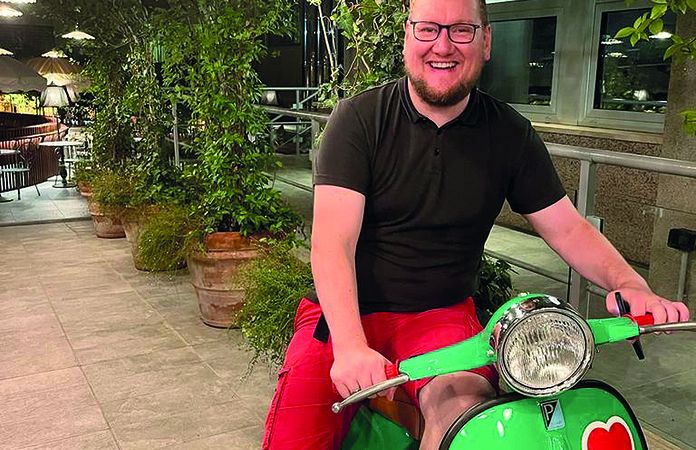 Stephan Anders-Krummnacker mit T-Shirt und jurzer Hose auf einer Piaggio Vespa