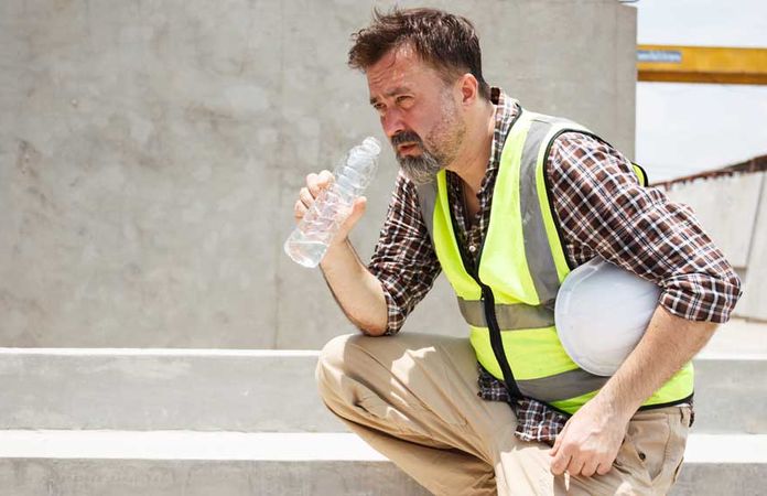 Ein Arbeiter mit Warnweste hockt und trinkt an einer Flasche Wasser